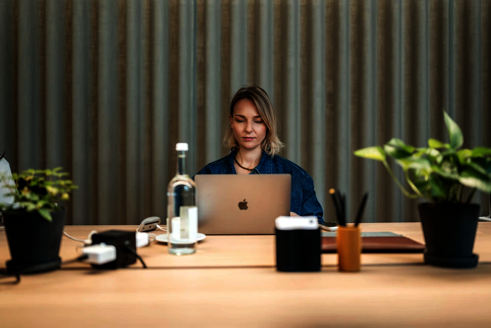 Frau arbeitet am Laptop an einem Holztisch mit Pflanzen im Office Club Berlin Kurfürstendamm