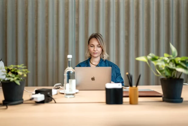 Frau arbeitet am Laptop an einem Holztisch mit Pflanzen im Office Club Berlin Kurfürstendamm