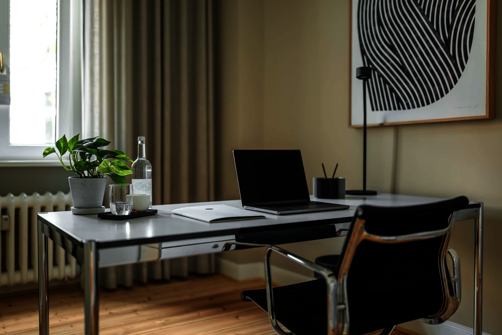 Schreibtisch mit Laptop, Pflanze und Wasserflasche am Fenster eines Einzelbüros im Office Club Berlin Kurfürstendamm