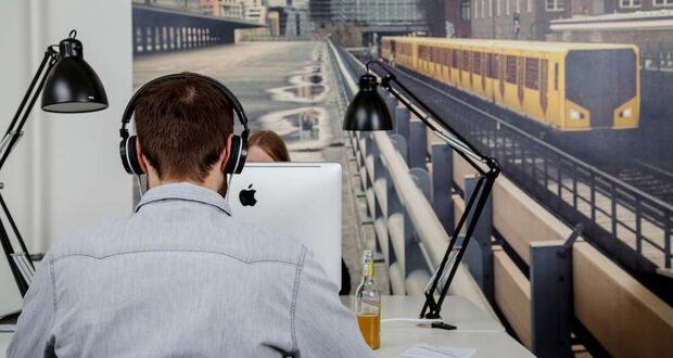 Mann mit Kopfhörern am Schreibtisch vor einem Wandbild mit U-Bahn