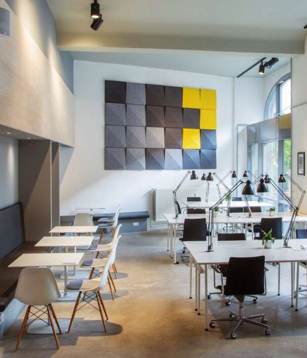 Coworking-Bereich mit Arbeitstischen und grau-gelben Akustikpaneelen im Office Club Berlin