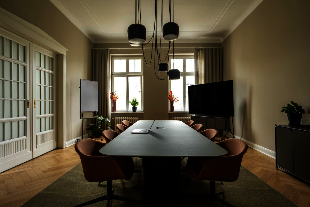 Meetingraum mit Konferenztisch, terracottafarbenen Stühlen, Bildschirm und Flipchart im Office Club Berlin Kurfürstendamm