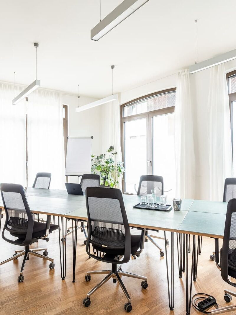 Großer Meetingraum mit langem Tisch, schwarzen Stühlen und Bildschirmen im Office Club Potsdam