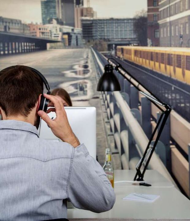 Mann am Telefon am Schreibtisch vor einem Wandbild mit U-Bahn