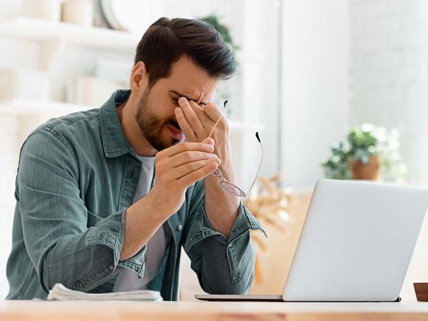 Mann sitzt vor seinem Laptop und reibt sich die Augen