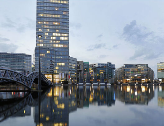 Das Hochhaus KölnTriangle und eine Rheinbrücke spiegeln sich in der Abenddämmerung im Rhein