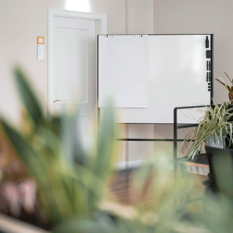 Meetingraum mit Whiteboard, im Vordergrund unscharfe Pflanzen, im Office Club