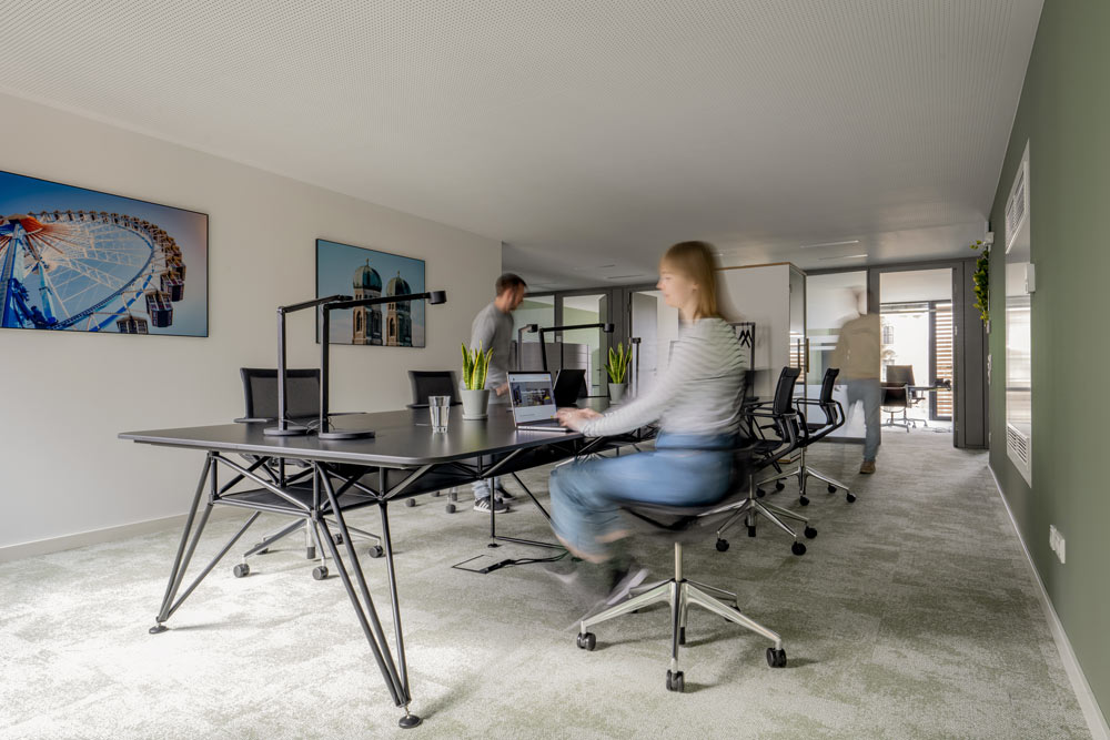 Open Space mit langen Arbeitstischen und arbeitenden Menschen im Office Club