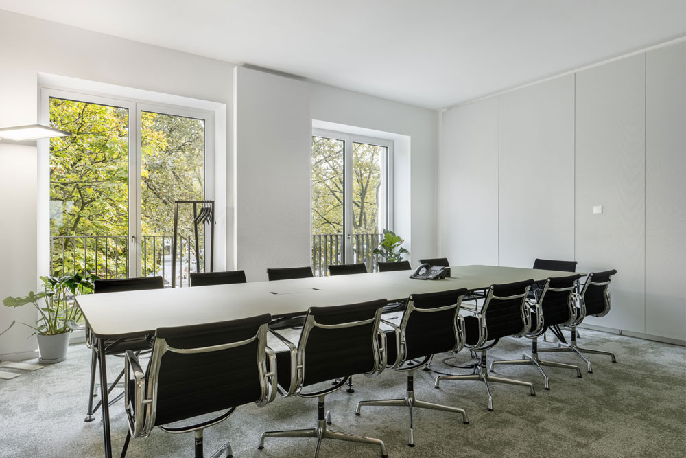 Konferenzraum mit langem Tisch, schwarzen Stühlen und Fenstern ins Grüne im Office Club Düsseldorf