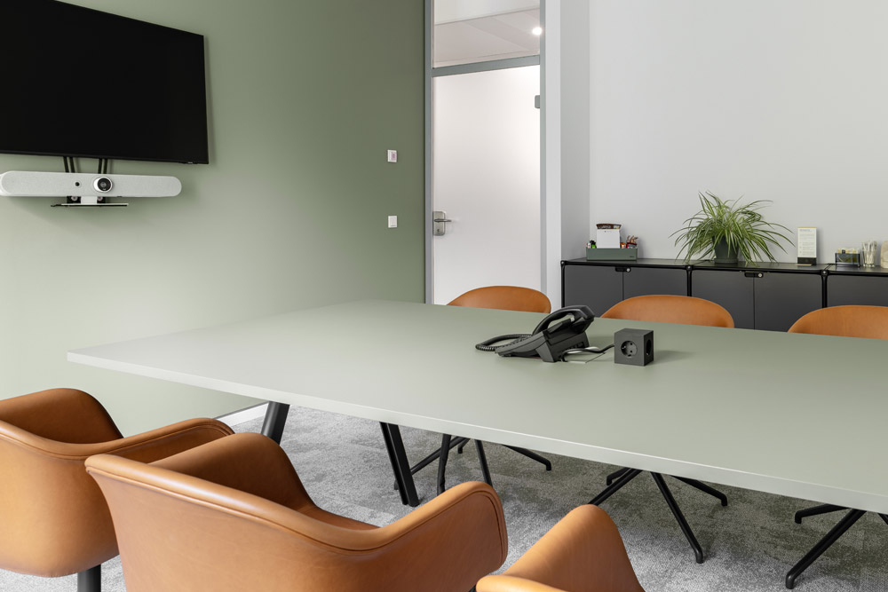 Meetingraum mit langem Tisch, cognacfarbenen Stühlen und Sideboard vor grüner Wand im Office Club Düsseldorf