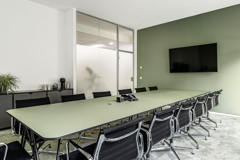 Seminarraum mit langem Tisch, schwarzen Stühlen und Bildschirm im Office Club Düsseldorf