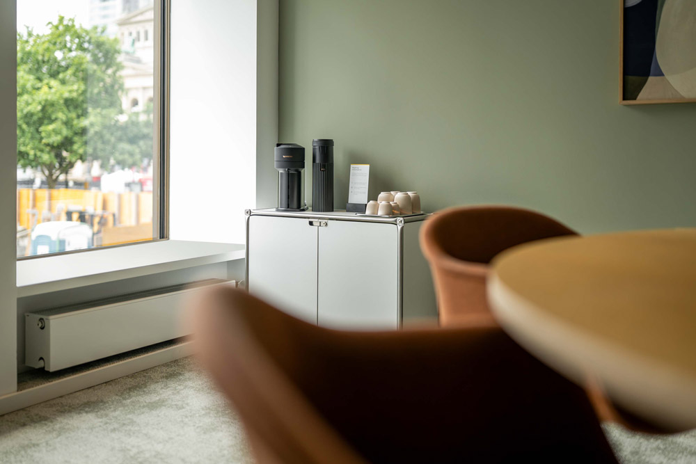 Runder Holztisch mit orangefarbenen Stühlen am Fenster im Office Club Frankfurt