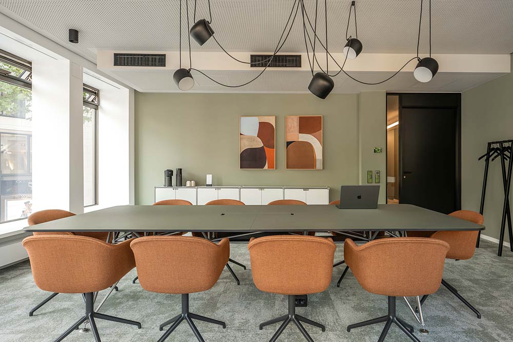 Konferenzraum mit langem Tisch, orangefarbenen Stühlen und Hängeleuchten im Office Club Frankfurt Goethestraße