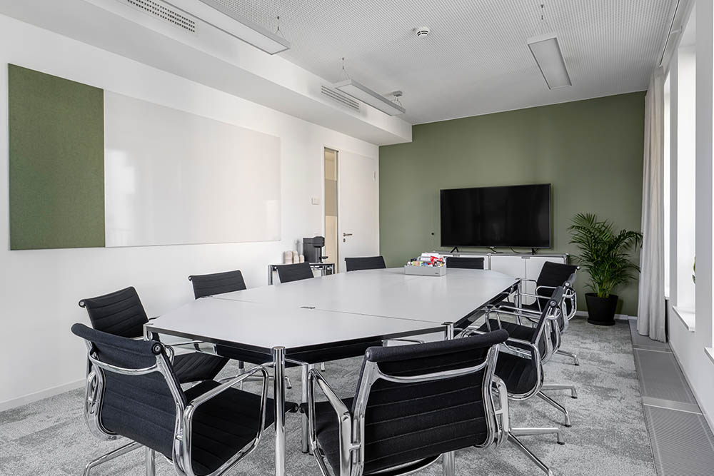 Tagungsraum mit langem Tisch, schwarzen Stühlen und Bildschirm vor grüner Wand im Office Club Hamburg