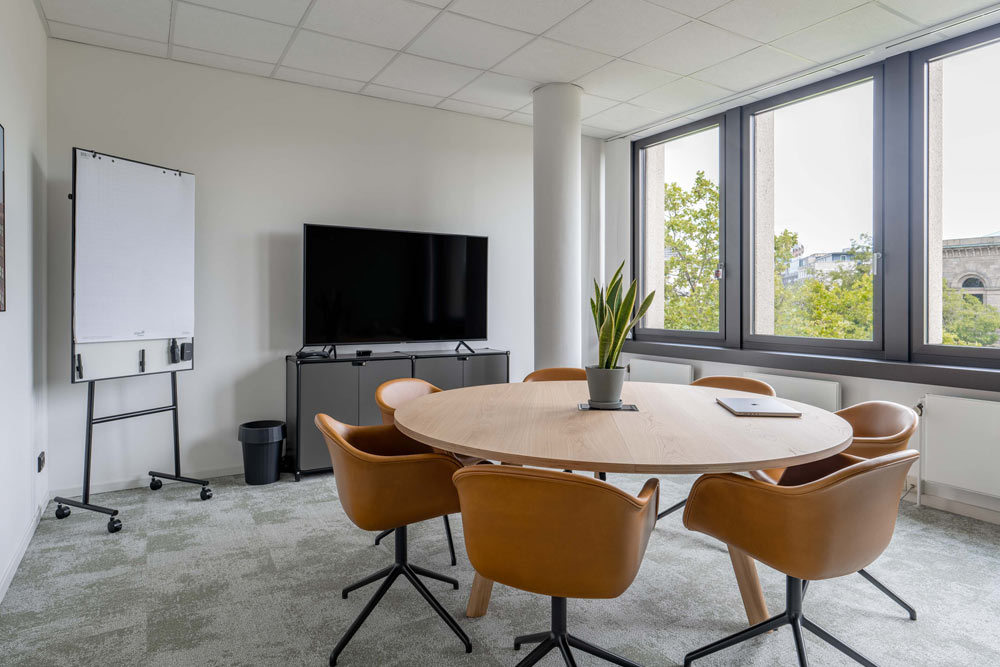 Kleiner Konferenzraum mit rundem Tisch, orangefarbenen Stühlen und Bildschirm im Office Club Hannover