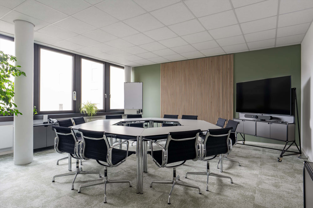 Konferenzraum mit Holzlamellenwand, schwarzen Stühlen und Bildschirm im Office Club Hannover