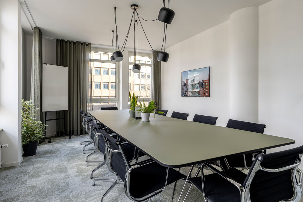 Konferenzraum mit langem Tisch, schwarzen Stühlen und Hängeleuchten im Office Club Köln