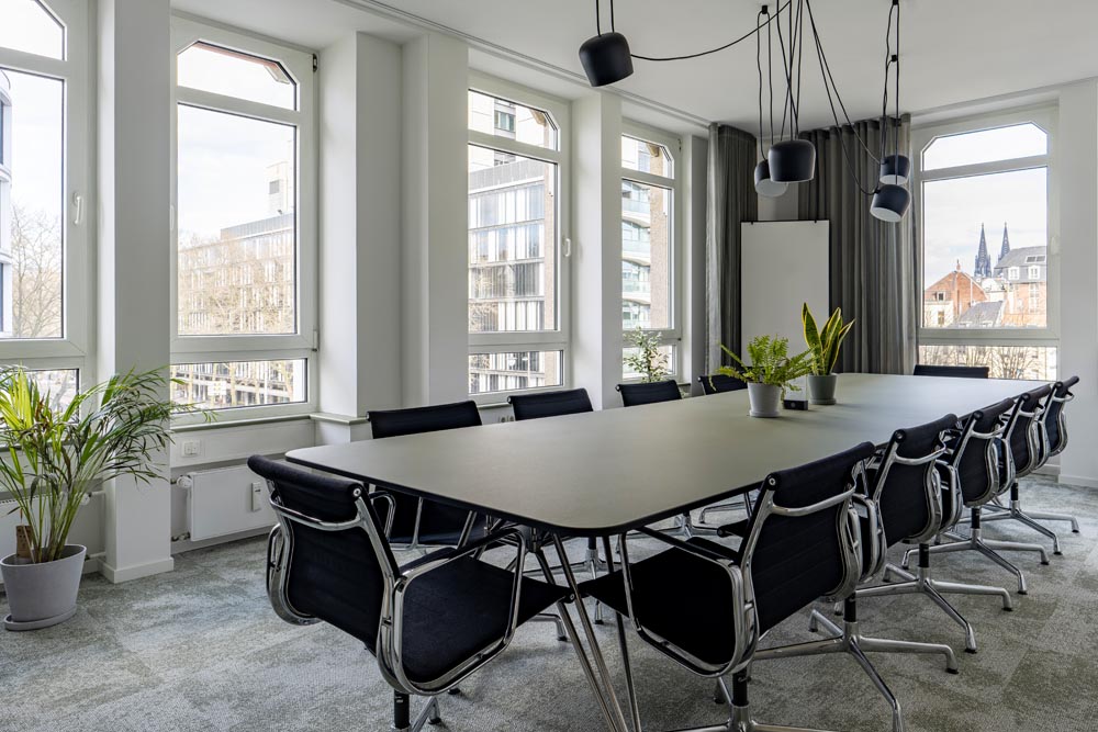 Konferenzraum mit langem Tisch und schwarzen Stühlen vor hohen Fenstern im Office Club Köln Hohenzollernring