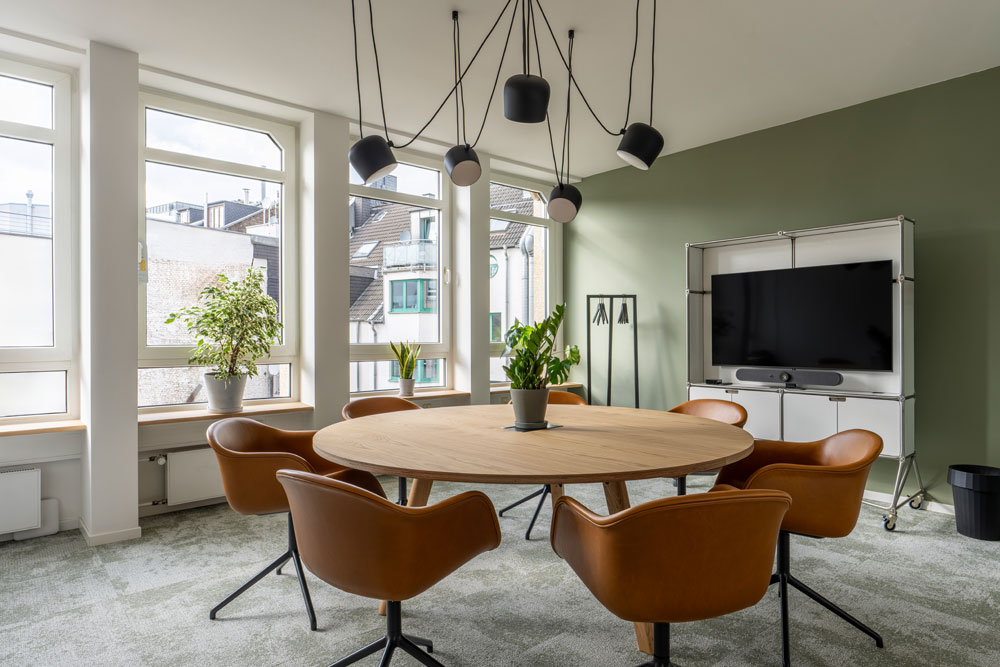 Besprechungsraum mit rundem Holztisch, cognacfarbenen Stühlen und Bildschirm im Office Club Köln Friesenplatz