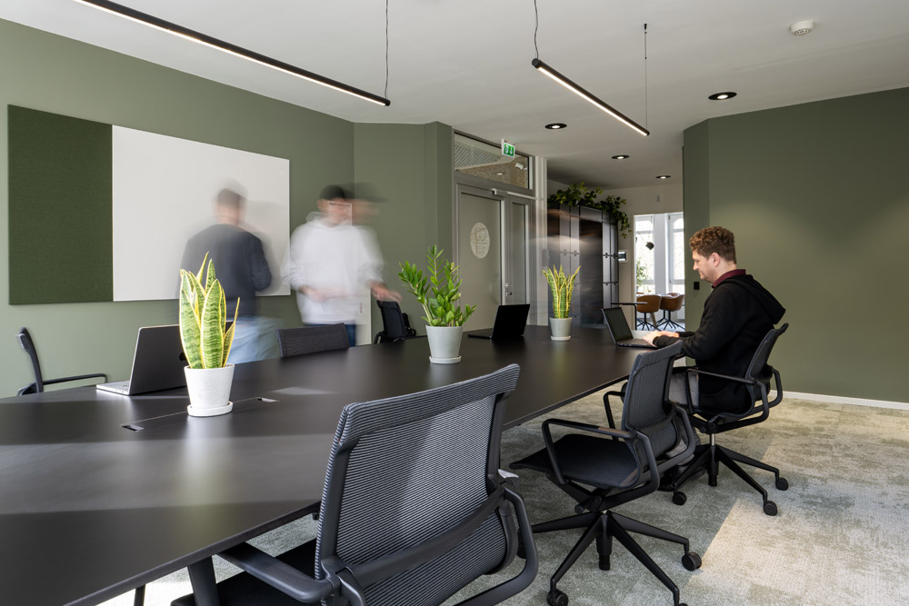 Menschen arbeiten am langen Tisch vor grüner Wand im Office Club Köln Hohenzollernring