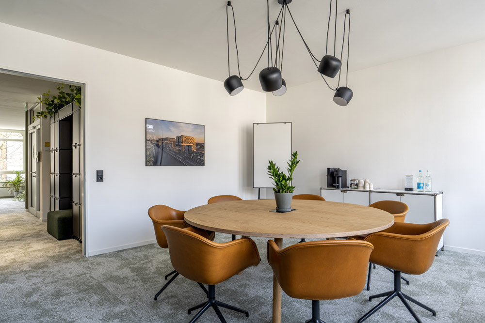 Moderner Konferenzraum mit rundem Tisch, cognacfarbenen Stühlen und Hängeleuchten im Office Club Köln