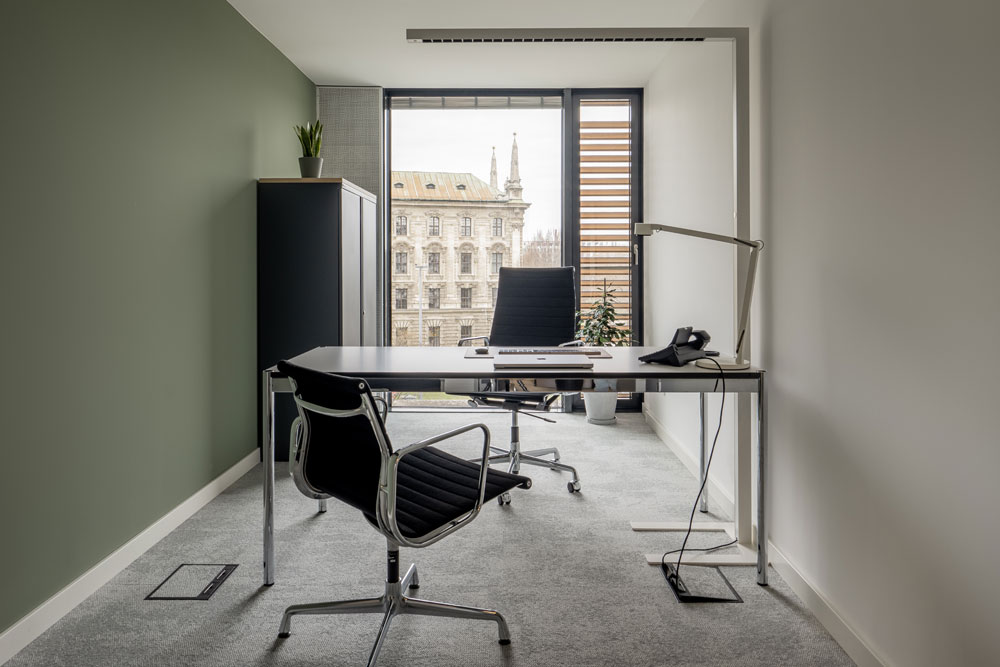 Büro mit Schreibtisch, schwarzem Bürostuhl und Fensterblick im Office Club München Stachus