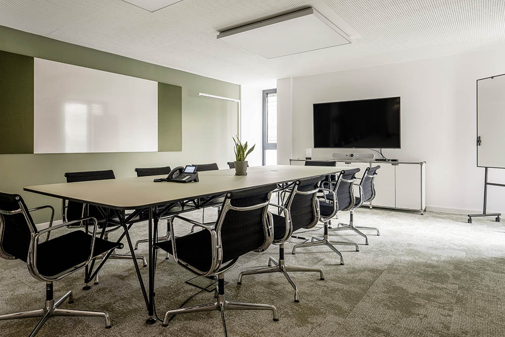 Konferenzraum mit langem Tisch, schwarzen Stühlen und Bildschirm im Office Club München