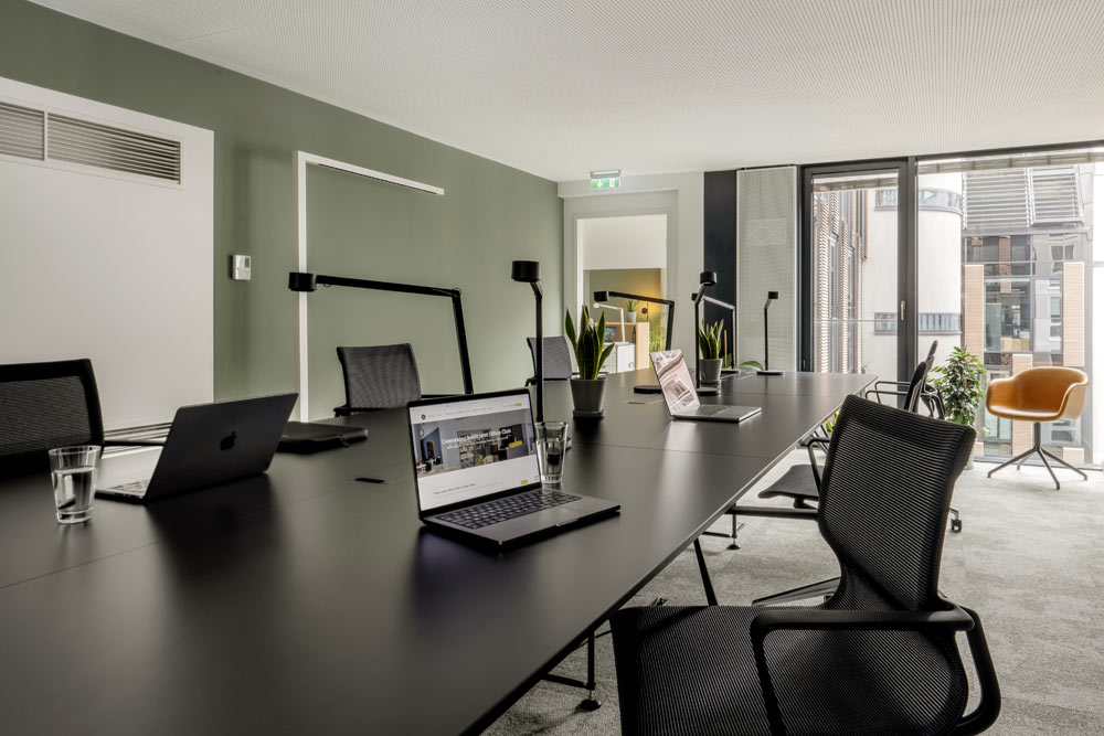 Coworking-Bereich mit langen schwarzen Tischen und Laptops im Office Club München Stachus