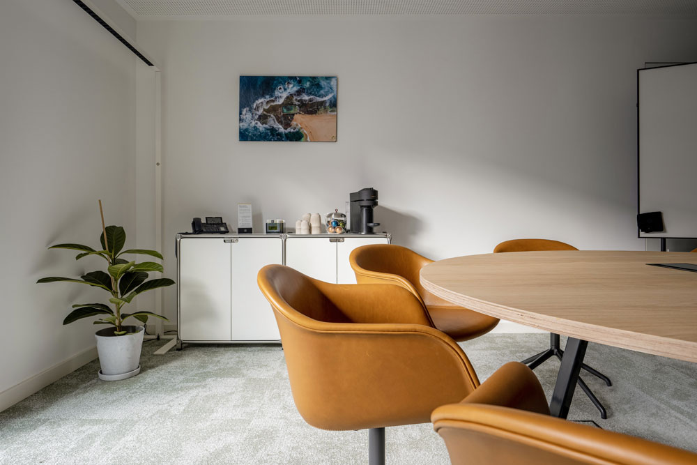 Konferenzraum mit rundem Tisch, cognacfarbenen Stühlen und Sideboard im Office Club München