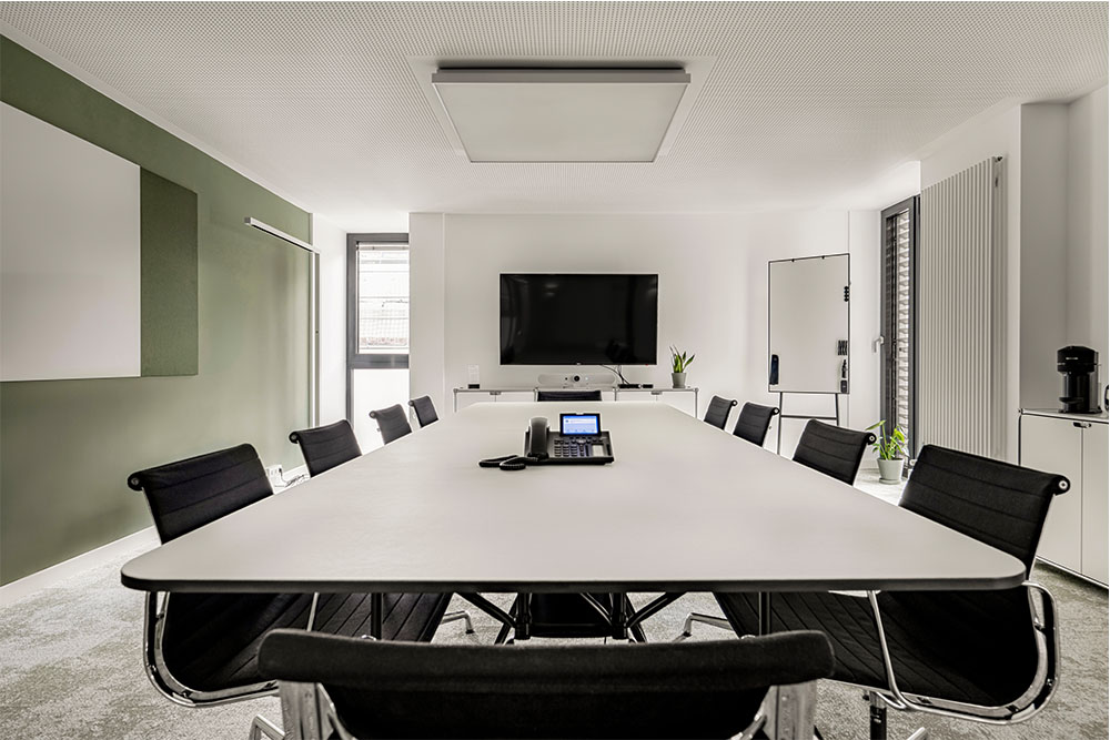 Konferenzraum mit langem weißem Tisch, schwarzen Stühlen und Bildschirm im Office Club München Stachus