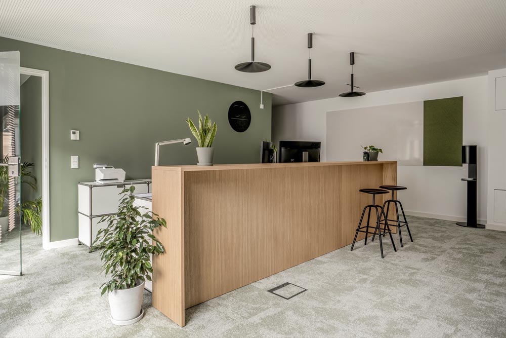 Empfang mit Holztheke und Barhockern vor grüner Wand im Office Club München Stachus