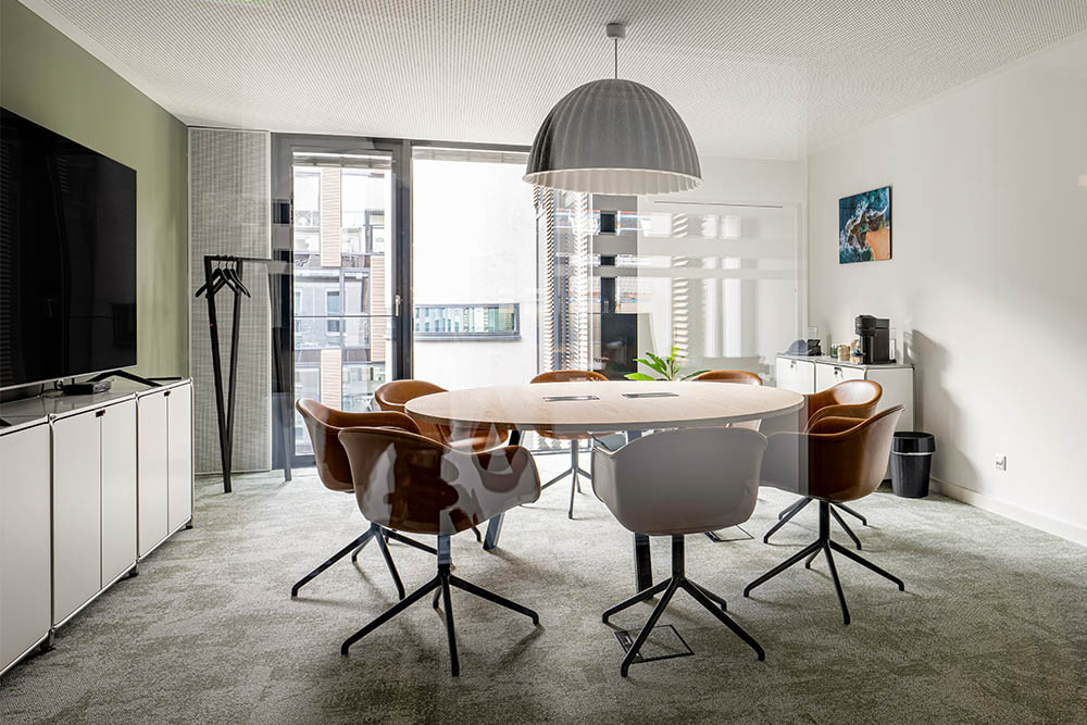 Seminarraum mit rundem Tisch, Hängeleuchte und Bildschirm im Office Club München Stachus