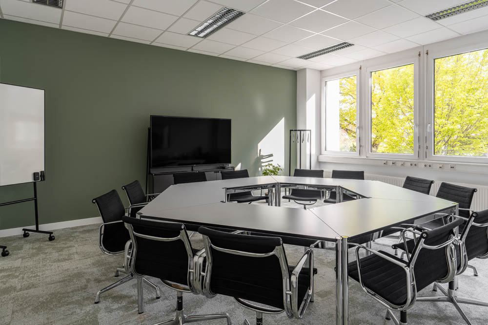 Meetingraum mit schwarzen Stühlen, Bildschirm und grüner Wand im Office Club Nürnberg