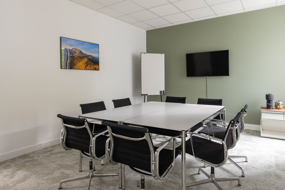 Veranstaltungsraum mit Tisch, schwarzen Stühlen, Bildschirm und Flipchart im Office Club Nürnberg