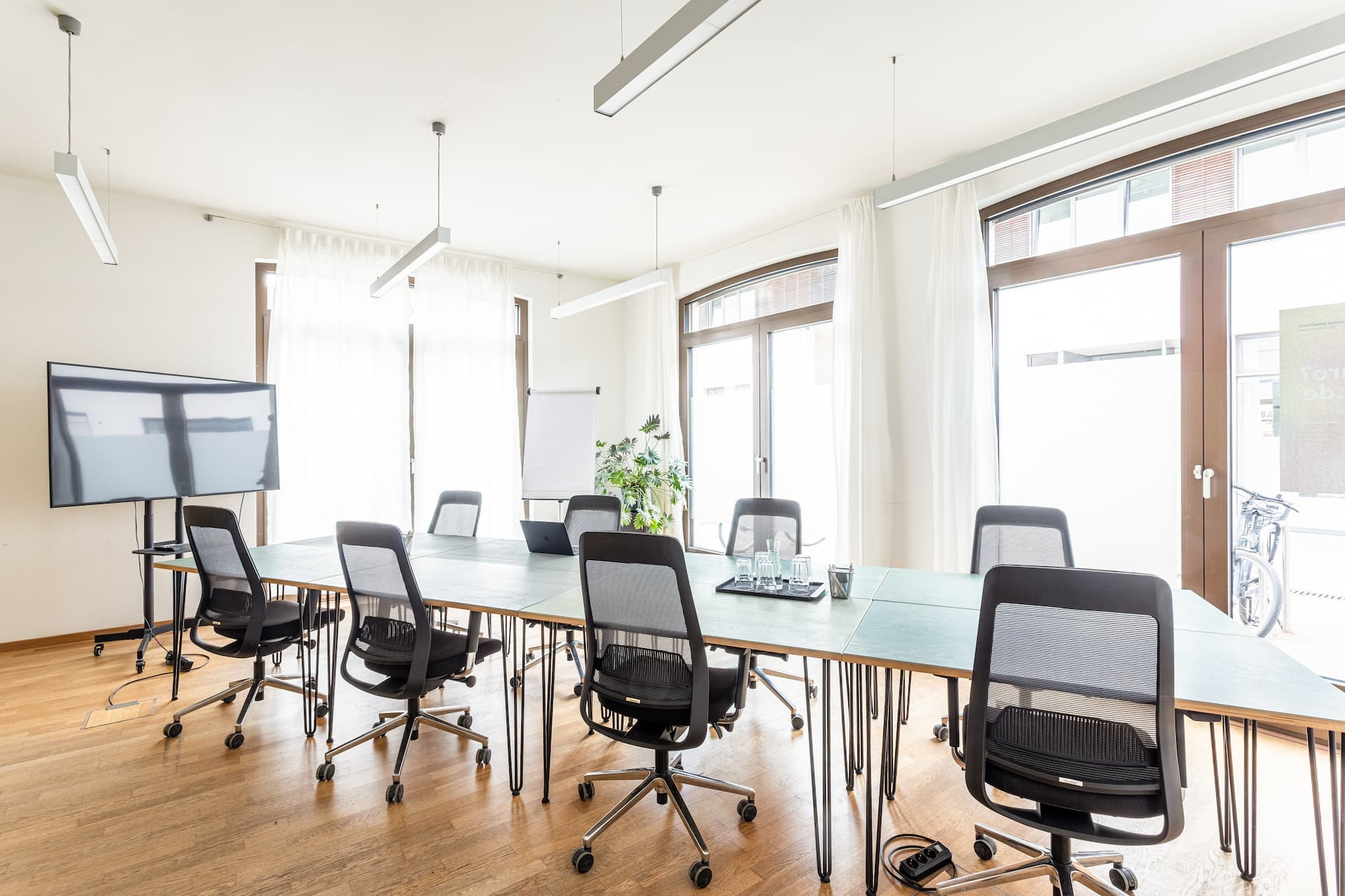 Großer Meetingraum mit langem Tisch, schwarzen Stühlen und Bildschirmen im Office Club Potsdam