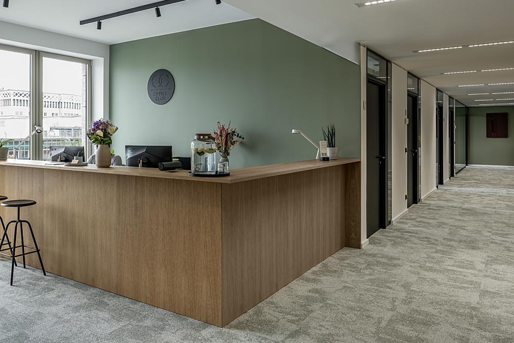 Empfang mit Holztheke und Blumen vor grüner Wand im Office Club Stuttgart