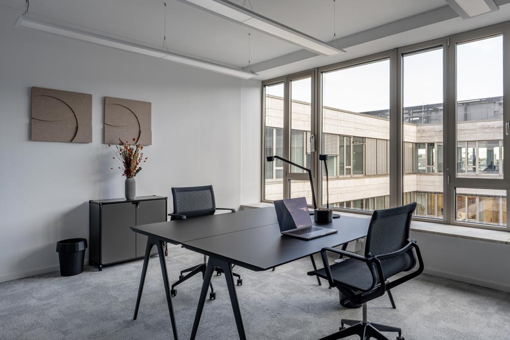 Teambüro mit Schreibtisch, Laptop und großen Fenstern im Office Club Stuttgart