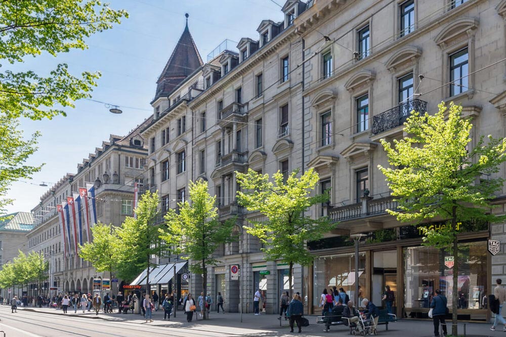Historische Geschäftshäuser an einer baumbestandenen Straße in Zürich