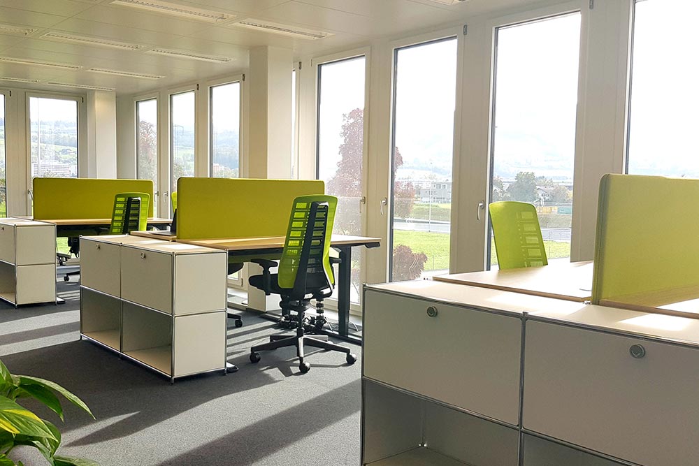 Coworking-Bereich mit Schreibtischen und hellgrünen Sichtschutzwänden im Office Club Zug