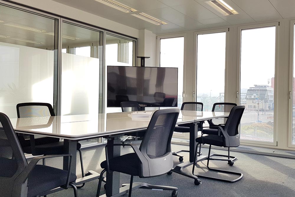 Sitzungszimmer mit langem Tisch, schwarzen Stühlen, Bildschirm und großen Fenstern im Office Club Zug