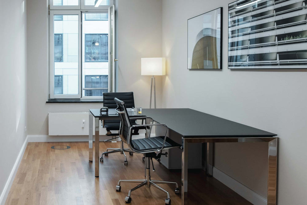 Helles Büro mit Schreibtisch, schwarzen Bürostühlen und großem Fenster im Office Club Berlin Mitte