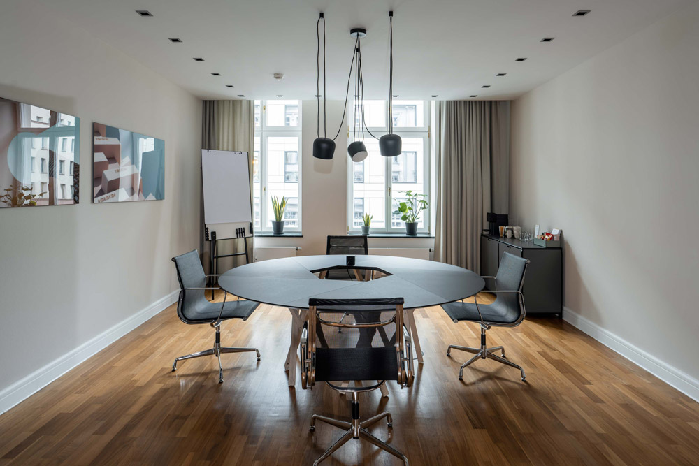 Konferenzraum mit rundem Tisch, schwarzen Bürostühlen und Flipchart im Office Club Berlin Französische Straße