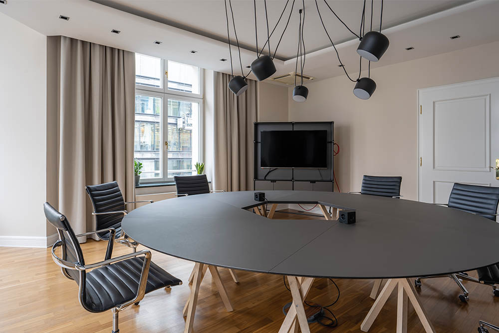 Meetingraum mit ovalem Tisch, schwarzen Stühlen und Hängeleuchten im Office Club