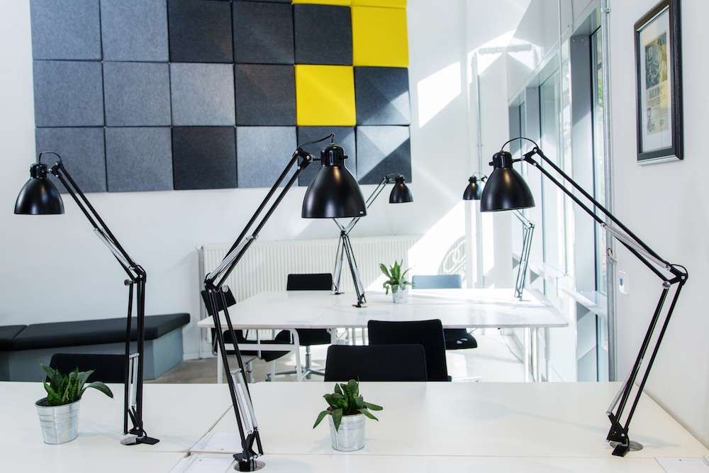Helle Arbeitsplätze mit schwarzen Schreibtischlampen und Akustikpaneelen im Office Club Berlin