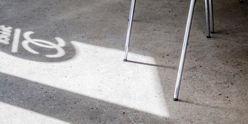 Sonnenlicht wirft das Office Club Logo als Schatten auf den Betonboden neben Stuhlbeinen