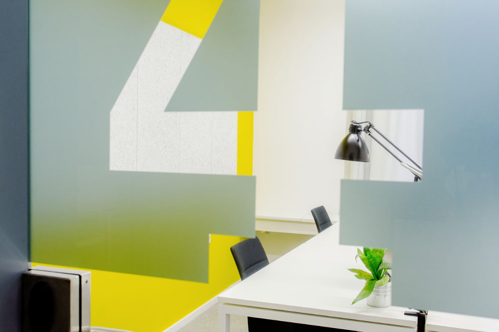Wandgestaltung mit großer Ziffer 4 in Grau und Gelb neben einem Arbeitsplatz