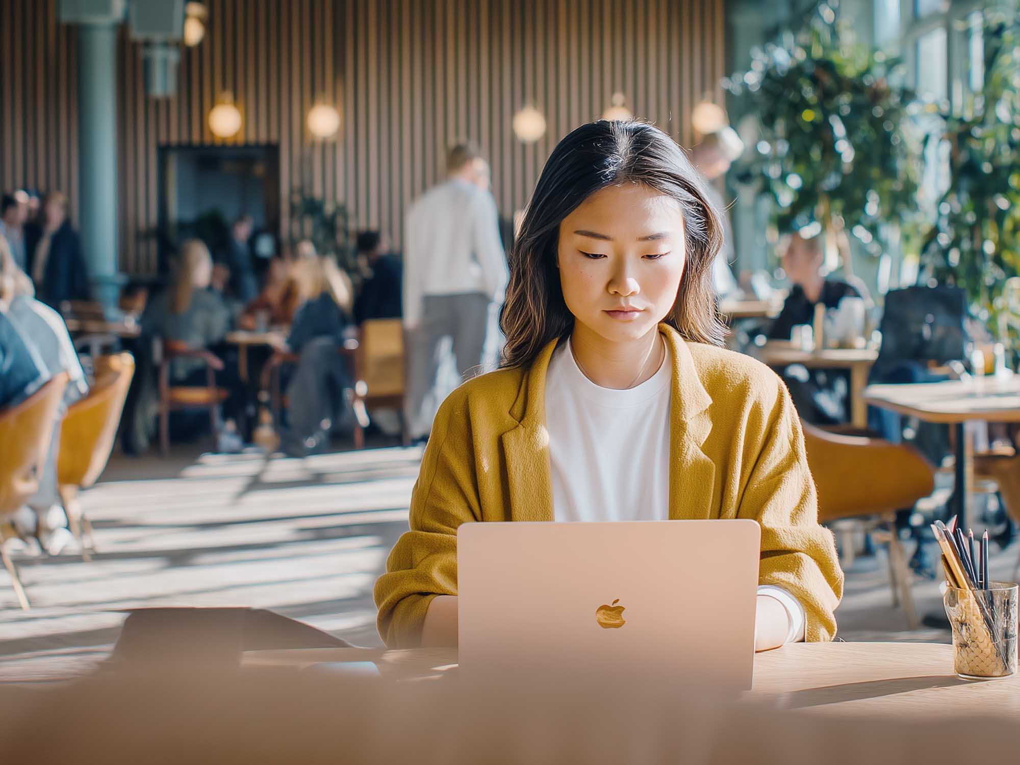 Junge Frau arbeitet konzentriert mit Laptop an einem Flex Desk in einem modernen Coworking Space mit hellen Räumen und lebendiger Atmosphäre.